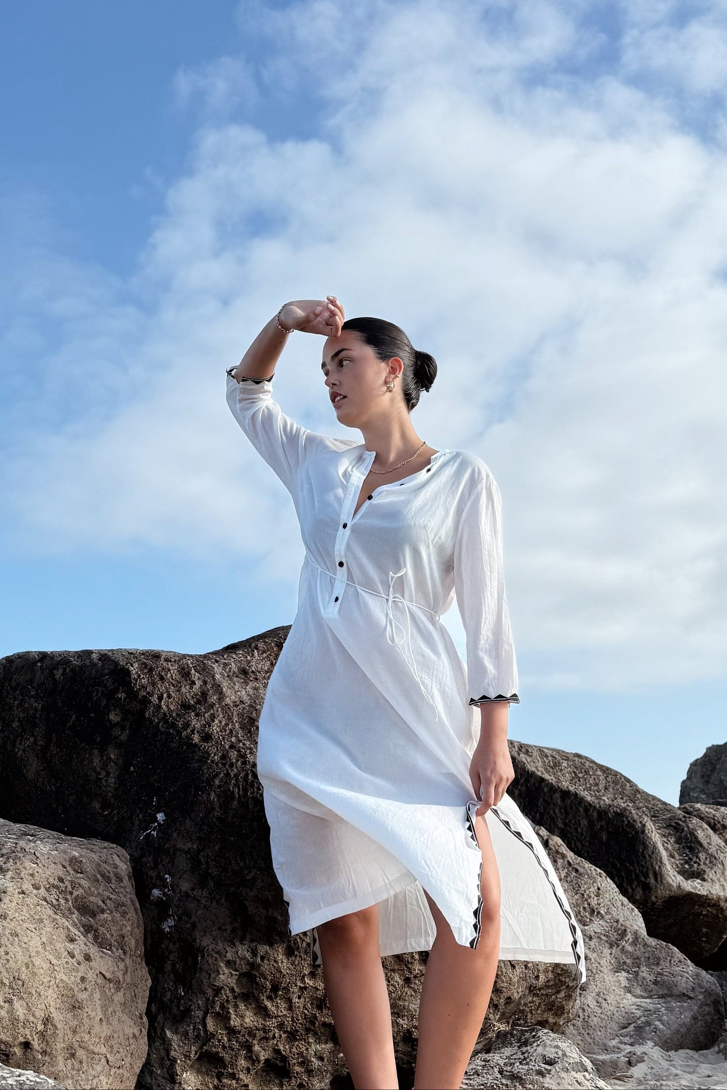 Woman in a white dress standing on rocks with a blue sky and clouds in the background